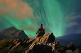 Woman sitting on a rock in front of the aurora borealis contemplating (source: Canva Pro)
