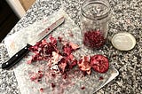 Messy deconstructed pomegranate and seeds with a knife on a kitchen counter