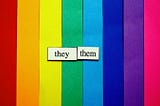 pride rainbow colors in strips of construction paper with they and them magnets laid on top