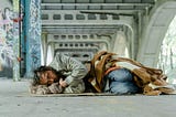 A homeless man lying outdoor under an overpass.