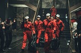 Armed robbers in red jumpsuits and Dali masks marching down stairs
