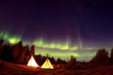 Two tents in an open area at night with green Northern Lights in the sky.