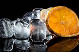 Ice cubes with a slice of orange against a black background