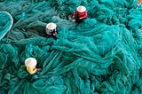 People working to repair and tend to vast fluffy piles of fine fish netting