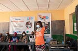 Esther Mark, known as Aunty Esther, in a hall with other participants at the No To DRUG ABUSE campaign rolled out by her team from YALI PLATEAU for secondary school students. She hold a mic and talks on the advocacy as other guests look on.
