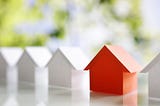 White small toy houses in a row and one is red.