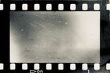 Burned black and white film strip with faint distortions and scratches against a white background.
