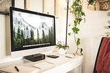 An Apple computer with blank sheets of paper on a white wooden desk.