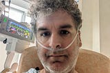 Author in intensive care with tubes inserted and monitors visible.