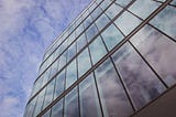 A glass and steel skyscraper shot from below, against a partly cloudy sky.