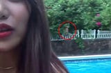 An Asian woman taking a selfie in daylight. In the background is an  apparation of a ghost staring over her shoulder.