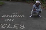 Rapper NGB QUIS squatting down wearing a white hat with a jean jacket