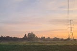 Sunrise over rural landscape including electricity pylon, trees and grass