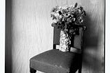 Black & White photograph of a bouquet of flowers standing on a chair.