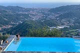 Woman sitting in a pool overlooking a town in Italy. Ocean is visible beyond.