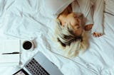 woman sleeping on a bed with laptop and open notebook nearby