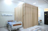 A hospital ward with a privacy curtain drawn around a patient’s bed.
