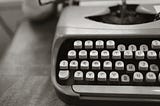An antique typewriter with a sheet of paper sitting on a wooden desk. Photo by Leah Kelley: https://www.pexels.com/photo/close-up-photo-of-gray-typewriter-952594/