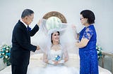 woman-in-wedding-dress-between-older man-in-formal-suit-and-older woman-in-blue-dress