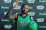 Photo of Damian Lillard wearing a “Hulu Doesn’t Have Live Sports” basketball jersey, holding a green ‘Hulu’ basketball & waving to the camera.