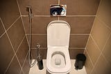 a toilet in Morocco with a small water gun next to it