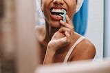 Woman in a bathroom mirror using a tooth flosser.