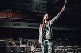 Young man waving an American flag in an old decaying empty theatre.