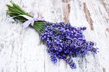 A bunch of lavender placed on a wooden surface, tied with a violet ribbon.