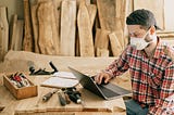 Carpenter working on his laptop surrounded by wood