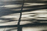 Filtered light casts soft, intersecting shadows on a tiled floor, creating a quiet pattern of presence and absence.