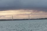 A suspension bridge over water under moody sky
