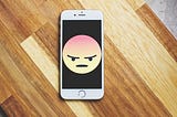 An white Apple iPhone with an image of an angry face emoji.