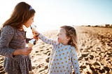 Little girl sharing ice cream with slightly older girl.