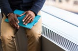 A Black job seeker’s hands rest on their lap on top of a tablet in a blue cover. They seem to be positioned as if the photo was taken while the person was explaining something.