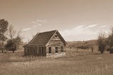 Sepia photo of an abandoned farmhouse in the prairie