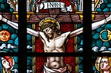 Photo of a blue and red stained glass window showing Jesus Christ hanging on the cross.