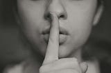 The image is a black-and-white photo of a woman putting her finger on her lips.