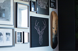 Image of a wall with artwork hanged including a skateboard and framed drawings.