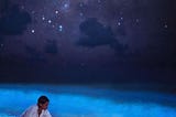 A woman scooping bioluminescent plankton with her hand at nighttime in the Maldives.