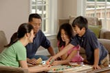 Family of four sitting around table playing Monopoly