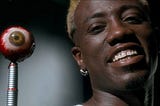 Photo of Wesley Snipes from the Movie Demolition Man smiling insanely and holding a fake eyeball on the end of a fountain pen to use as a biometric pass.