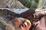 K. Asian American woman smiling with lips pursed and eyes close while basking in sunshine with sunspots in the photo