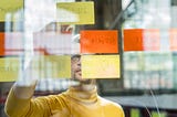 The author, Konrad Weber, stands in front of a glass wall with post-its on it.