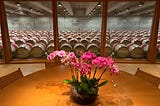 An orchid on a table with wine barrels behind the window