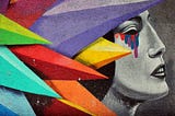 Progile black and white graffiti of woman crying with rainbow colored tears. She is peaking through rainbow colored spikes in the foreground.