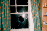 A broken window pane. There is a large hole in the window surrounded by cracks in the shatter-proof glass.