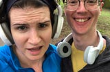 Two white people — on the left is a white, femme, white person wearing headphones and looking exasperated. On the right is a white man with glasses and headphones around his neck looking very happy.