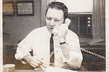 Classic 1960s man working the phones for the DNC in November 1961. He has on a white work shirt, tie, and is using a landline.