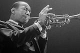 Lee Morgan, an African American man, is wearing a suit and playing a trumpet