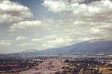 An Aztec pyramid is in the centre of the photo, sorrounded by scarce vegetation, with some mountains in the distance.